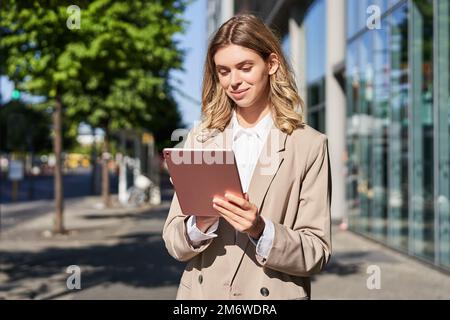 Portrait of corporate woman using her digital tablet, working and walking on street, going to office, multitasking Stock Photo