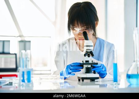 Scientist looking through a microscope working in science laboratory Stock Photo