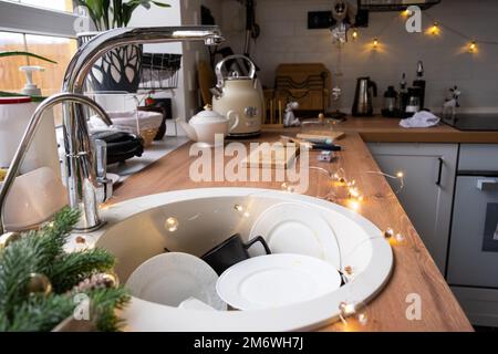 Dirty dishes in the sink in the garlanded kitchen, a holiday after a feast at Christmas. Mess after Stock Photo