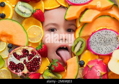 Kid licking melon. Vitamins from fruits. Mix of fruits near kids face. Assorted mix of summer fresh fruits. Healthy nutrition for kids. Stock Photo