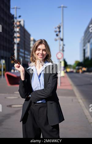 Portrait of successful young company ceo, businesswoman in black suit, standing on sunny street and smiling Stock Photo