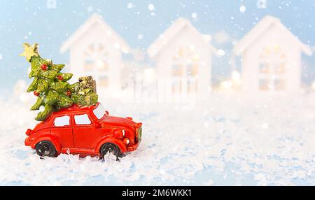 Christmas decor - red retro car on snow carries past white houses with lights garlands in bokeh Chri Stock Photo