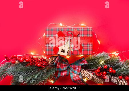 House key with keychain cottage on a festive background with Christmas tree, lights of garlands. Happy New Year-red background, Stock Photo