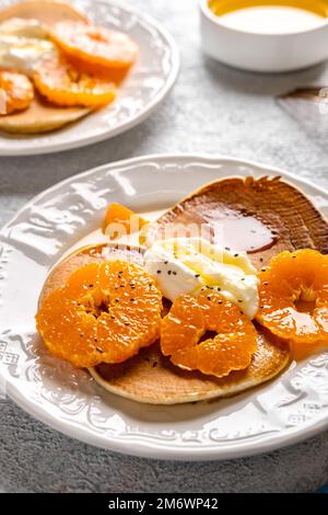 Close-up delicious pancakes with tangerines and honey or maple syrup for breakfast on a light background. Stock Photo