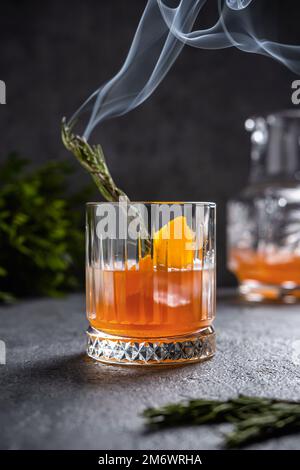 Negroni with smoking rosemary. Negroni with ice and orange on a dark background. Negroni cocktail in a glass with smoking rosema Stock Photo