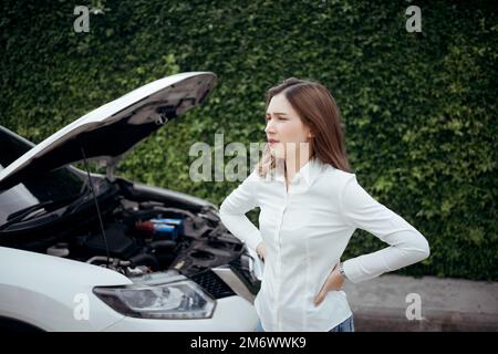 Young woman having car troubles - broken down car on the side of the road, calling the insurance company for assistance. Stock Photo