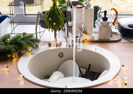 Dirty dishes in the sink in the garlanded kitchen, a holiday after a feast at Christmas. Mess after the guests for the New Year, Stock Photo