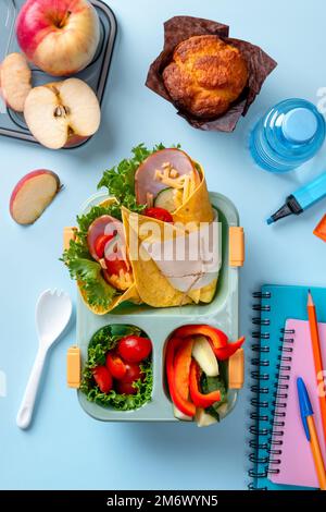 School lunch box for kids with sandwich, vegetables, water and stationery on table. Healthy eating habits concept. Back to schoo Stock Photo