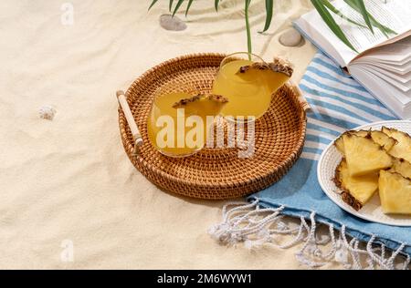 Cold pineapple cocktails on a wicker tray on beach with white sand. Summer sea vacation and travel concept. Exotic summer drinks Stock Photo