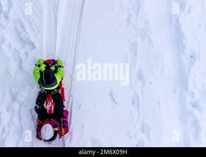 Aerial overhead done photo of two children in a sled going down a snow covered hill.  Stock Photo