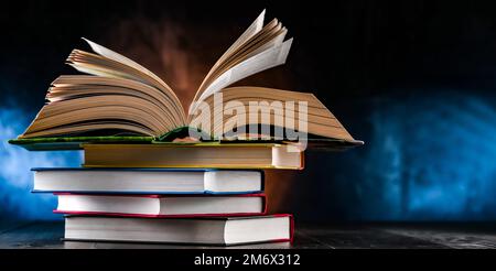 A composition with an open book lying on a stack of other books Stock Photo