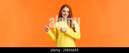 Time to prepare for holidays. Cheeky gorgeous smiling girl with red curly hair, pointing right, advice what shop visit, recommen Stock Photo