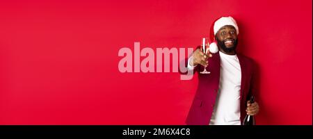 Christmas, party and holidays concept. Handsome Black man in santa hat raising glass of champagne and smiling, saying toast, cel Stock Photo