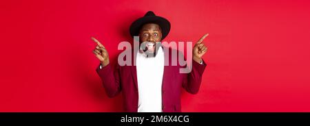 Winter holidays and shopping concept. Cheerful Black man smiling and showing two promo, pointing fingers sideways at copy spaces Stock Photo