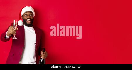 Christmas, party and holidays concept. Handsome Black man in santa hat raising glass of champagne and smiling, saying toast, cel Stock Photo
