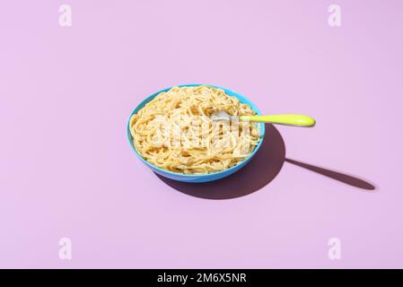Classic italian dish, spaghetti with parmesan cheese and black pepper, minimalist on a purple table. Pasta cacio e pepe in bright light on a vibrant c Stock Photo