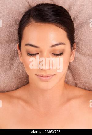 Letting her cares drift away. A beautiful young woman lying on a bed at a day spa with her eyes closed. Stock Photo
