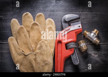 Adjustable wrench plumbing fittings leather protective gloves on wooden board. Stock Photo