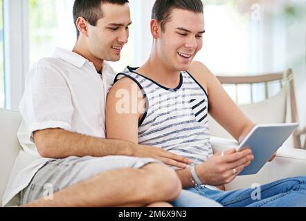 I cant believe they posted that photo of us. a young gay couple relaxing on the sofa at home with a digital tablet. Stock Photo