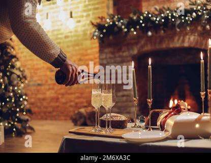 Man pouring champagne into glasses standing on table with festive dinner, candles and New Year gifts Stock Photo