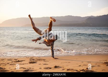 Getting his breakdance on. a young man dancing on the beach. Stock Photo