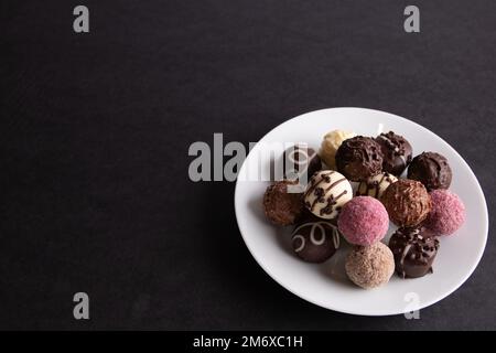 photo round multicolored chocolate sweets in a plate on a black background Stock Photo