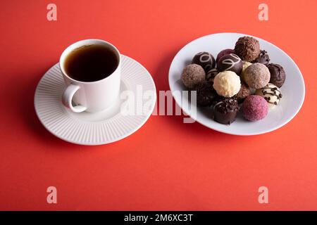 photo cup with coffee and different chocolates in a plate on a red background Stock Photo