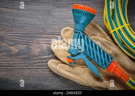 Garden rubber hose water sprinkler safety gloves on wooden board gardening concept. Stock Photo