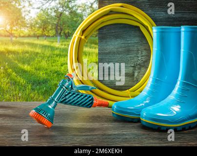 gardening tools watering hose with spray gan rain rubber boots on terrace in spring sunny garden Stock Photo