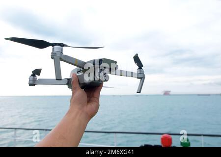 Hand reaching for drone outdoors at sunrise. Testing an aerial unmanned vehicle in nature. Sky background Stock Photo