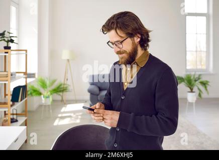 Bearded Caucasian man dressed in business-casual style with smile holding mobile phone Stock Photo