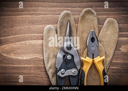 Composition of steel cutter pliers safety gloves on wooden board. Stock Photo