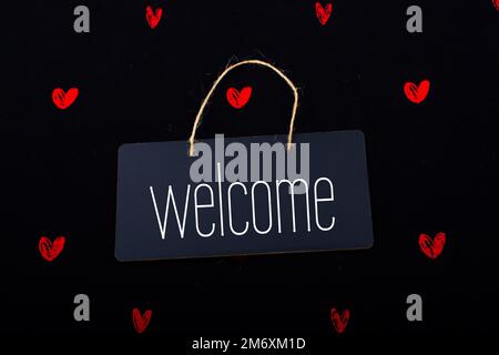 Welcome on black notice board  with red hearts around Stock Photo