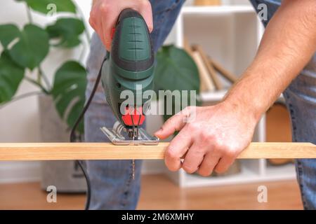 The hands of a master carpenter with an electric jigsaw in his hands cutting off a piece of wood. Male hands using fret saw for cutting wood. A carpen Stock Photo