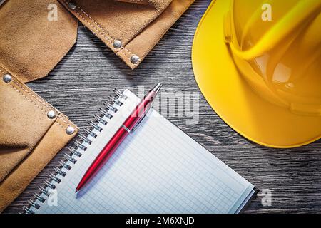 Leather tool belt protective hard hat checked notepad pen on wood board. Stock Photo