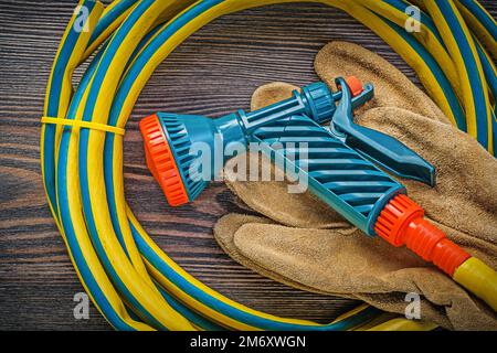 Hand spraying garden rubber hose safety gloves on wood board agriculture concept. Stock Photo