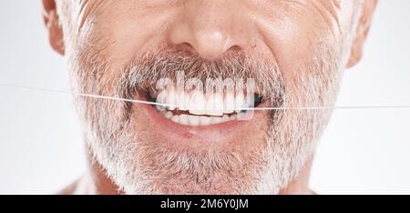 Dental, floss and mouth of senior man in studio isolated on a gray background. Hygiene, cleaning and elderly male model with product flossing teeth Stock Photo