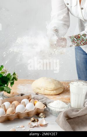 Female Hands Clapping Making Flour Splash above the Dough over Light Background. Eggs and Ingridients are on the Foreground. Empty Space for Text Stock Photo