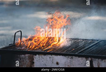 front view of metallic large old barbeque grill with fire flames and smoke coming out Stock Photo