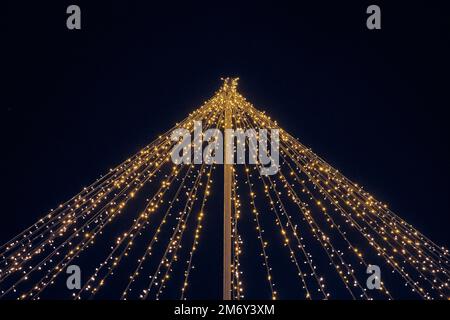 Yellow lights garlands outdoor hanging wires from pillar at night blue sky background, magic holiday atmosphere. Festive Christmas garlands with lumin Stock Photo