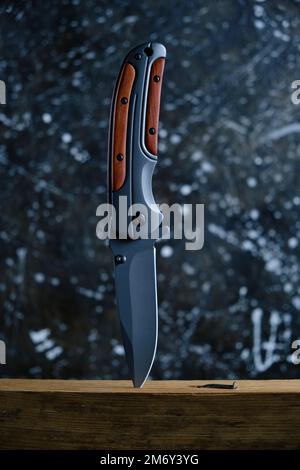Folding knife for survival stuck wooden beam, on dark background Stock Photo