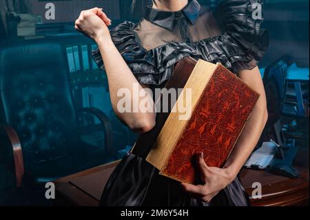 Old book in woman's hands close up. Woman holds an antique book in her hands. Closed book with aged pages. Stock Photo