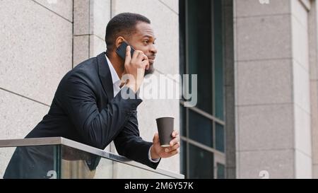 Serious bearded African American millennial businessman entrepreneur man ethnic manager talking mobile phone standing on office balcony male executive Stock Photo
