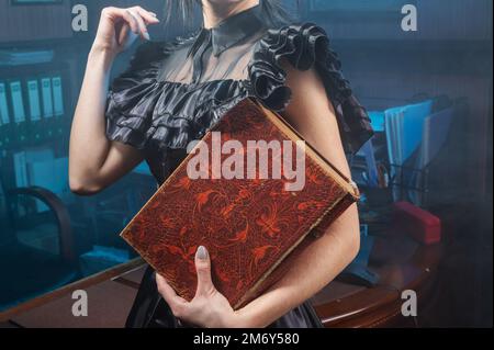 Old book in woman's hands close up. Woman holds an antique book in her hands. Closed book with aged pages. Stock Photo