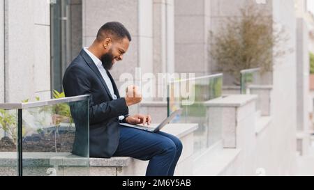 African American successful ethnic guy worker man entrepreneur executive employer ethnic businessman working with laptop outdoors near company office Stock Photo