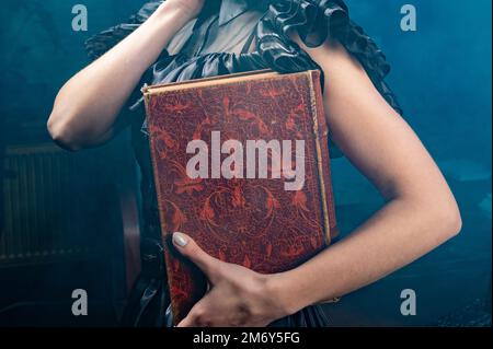 Old book in woman's hands close up. Woman holds an antique book in her hands. Closed book with aged pages. Stock Photo