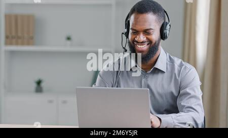Smiling happy African American ethnic businessman worker support help line agent manager online service worker teacher in headset man in office talk Stock Photo