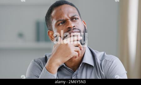 Pensive ethnic bearded African American man thinking businessman searching solution of difficult problem boss think ponder business strategy dreaming Stock Photo