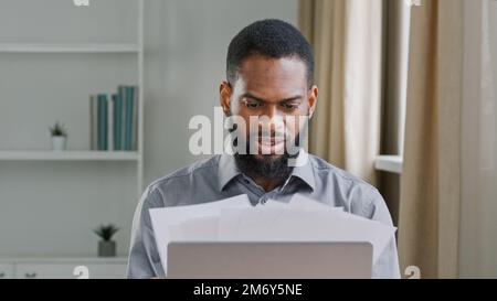 Pensive millennial ethnic bearded male office worker analyzing paperwork. Serious African American businessman leader man employer working with papers Stock Photo