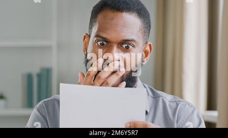 Unhappy African American shocked stressed bearded guy man in office reading bad news letter with bank credit loan refuse feeling stressed about Stock Photo